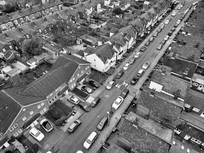 A quiet residential street scene depicting a narrow access area suited for house removals and home relocation logistics. The image shows a row of traditional brick houses with pitched roofs, some with